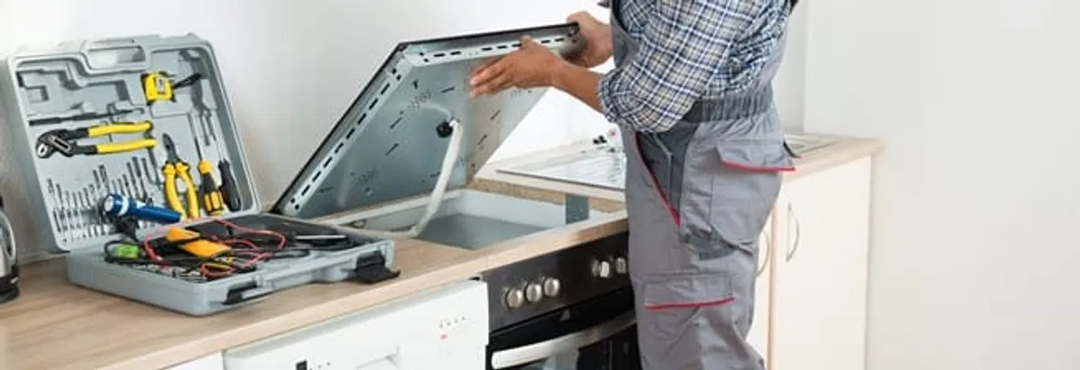 Cooktop repair technician lifting a built-in stovetop for service in Syracuse, NY