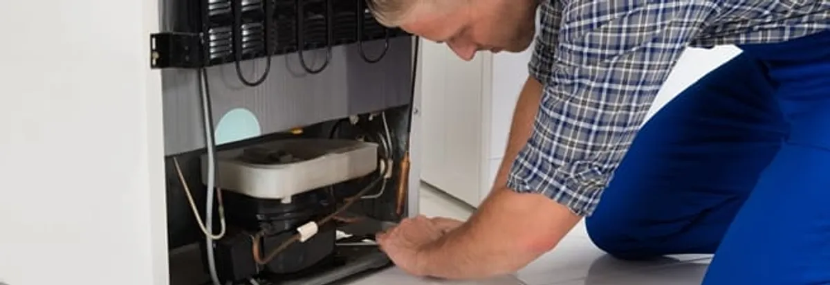 Refrigerator repair technician servicing the compressor and condenser area in Syracuse, NY