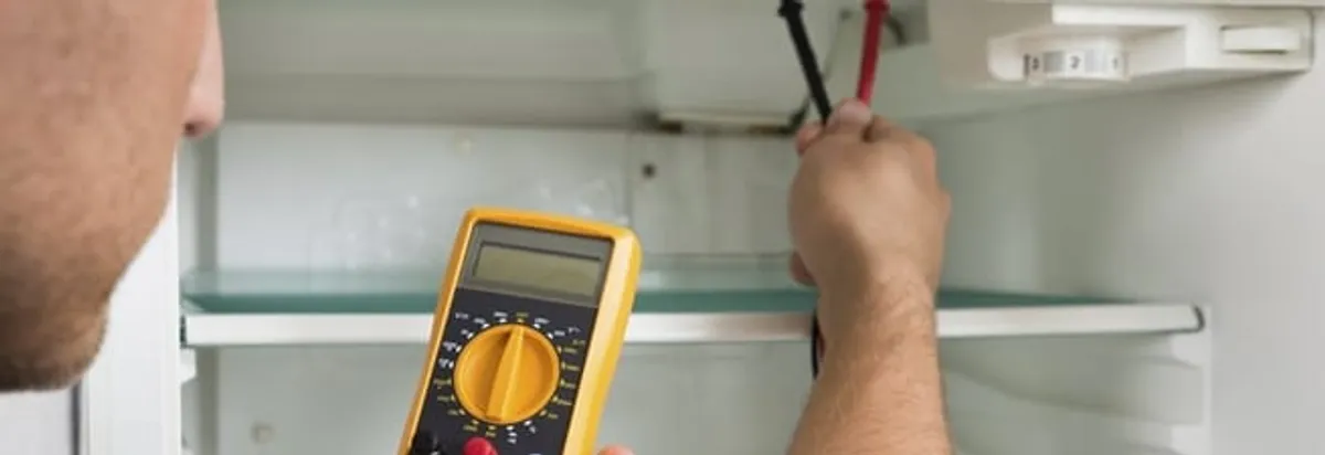 Refrigerator repair technician testing electrical components with a multimeter in Syracuse, NY